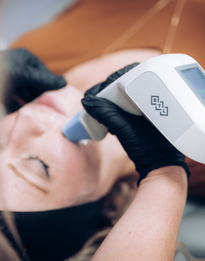 A woman receives a facial treatment from a medical professional using a handheld device.