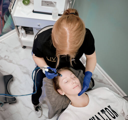 A technician performing a facial treatment on a client lying down, using advanced skincare equipment.