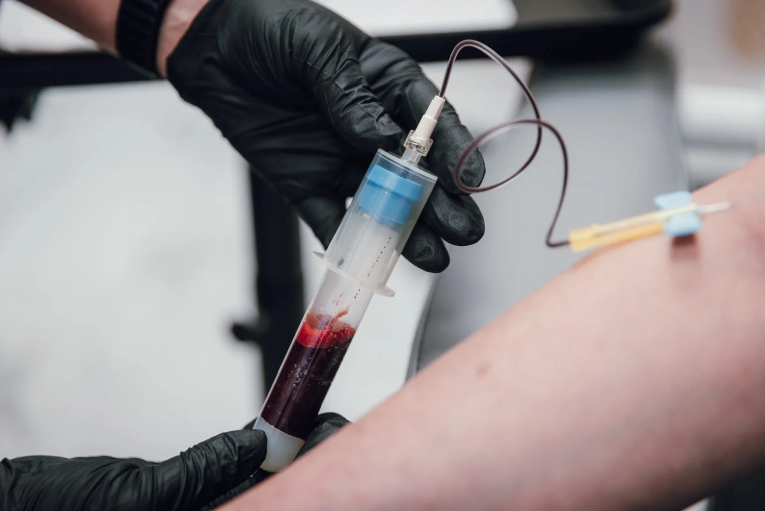 Healthcare professional wearing gloves drawing blood from a patient's arm using a syringe.