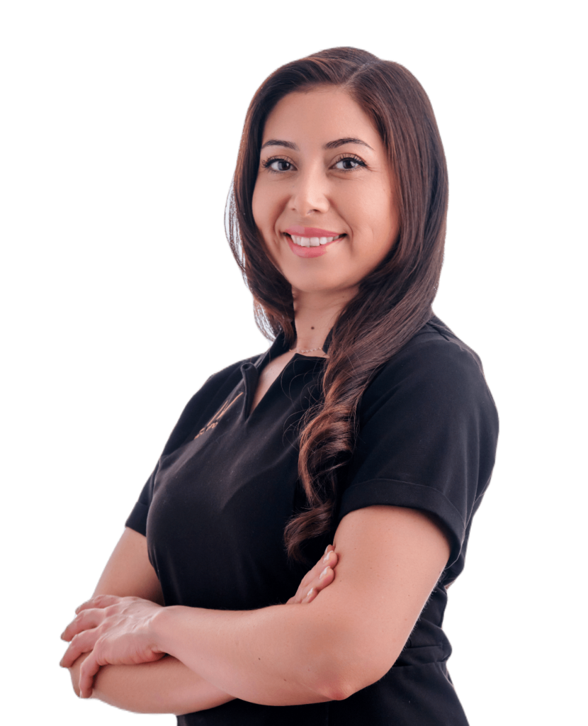 A professional woman named Denise stands confidently with her arms crossed, smiling while wearing a black polo shirt. She has long, styled hair and presents a friendly and approachable demeanor.