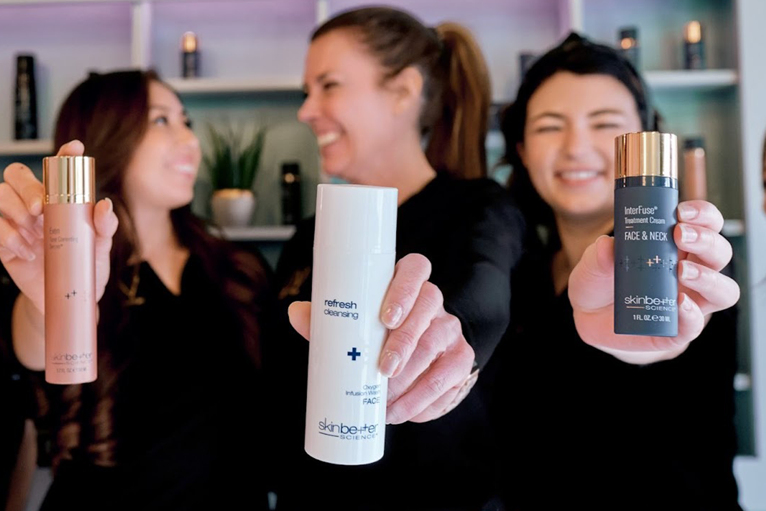 A group of smiling women in the background, slightly out of focus, with skincare products in the foreground. The scene captures a lively and friendly atmosphere, possibly at a beauty or skincare clinic, with the women appearing to enjoy their experience.