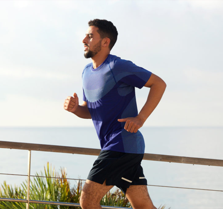 A man jogging outdoors near the ocean, wearing a blue athletic shirt and black shorts.