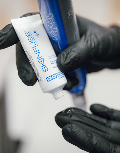 A gloved hand applies a clear skincare product to another gloved hand.