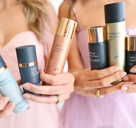 Two women holding an assortment of skincare products, including serums and creams, in their hands.