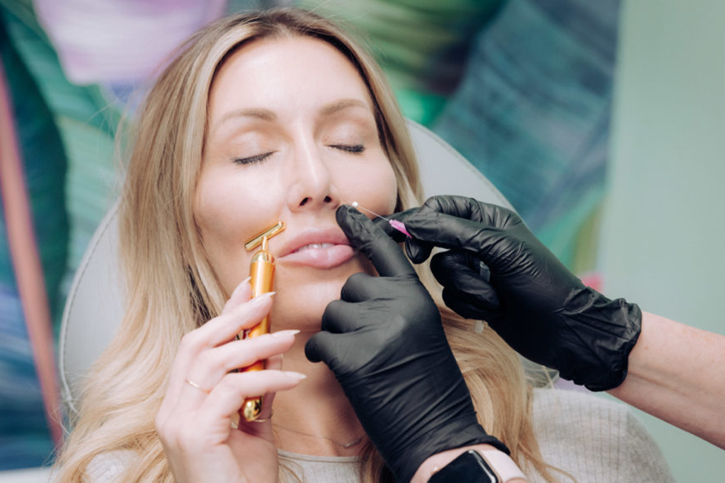 A woman receiving a cosmetic treatment with a roller massager and an injectable from a professional wearing black gloves.