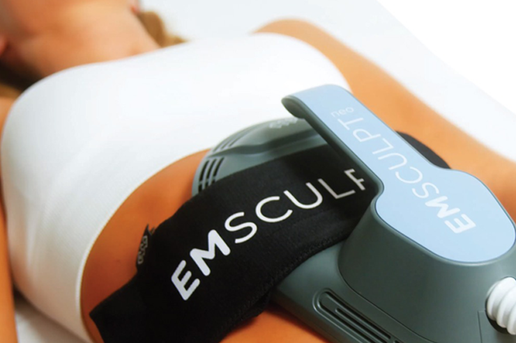 A woman undergoing an EMSCULPT neo treatment, with the device placed on her abdominal area.