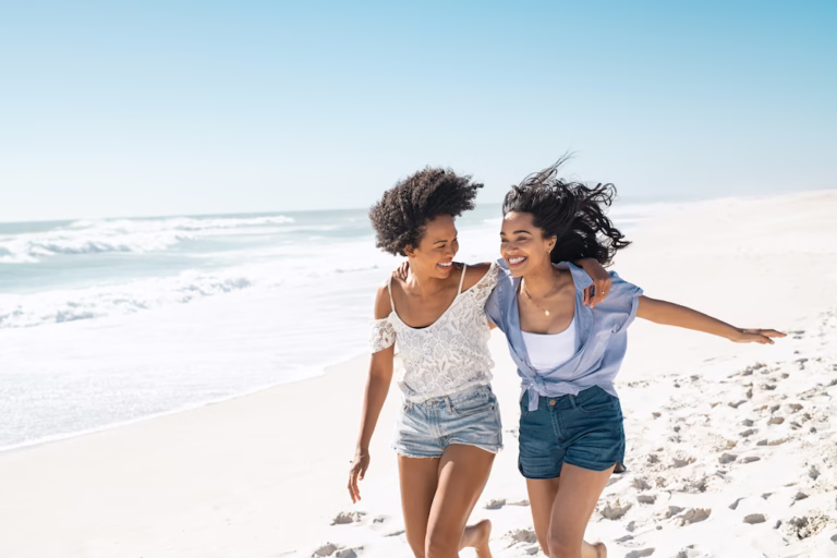 Happy women friends running on summer beach with copy space